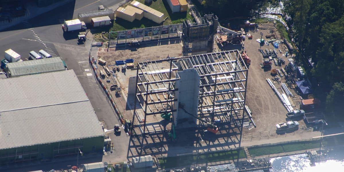 Aerial view of a new theme park attraction being built, showing the steel framework taking shape and colorful construction materials scattered around the site.