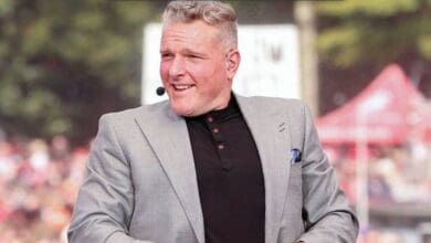 A lively theme park host in a sharp gray suit and headset microphone sits outside, engaging the excited audience as families gather in the colorful plaza behind him.
