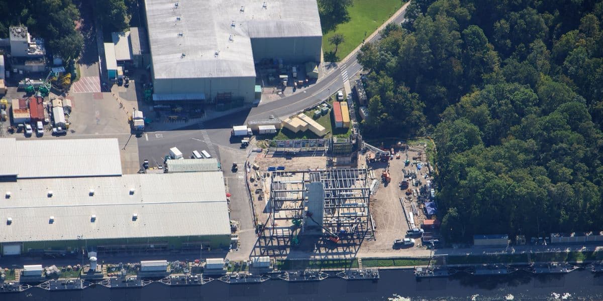 Aerial view of new roller coaster tracks being assembled near expansive theme park attractions and a nearby forested area.