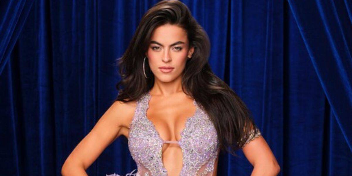 A glamorous performer in a sparkling, low-cut dress strikes a confident pose against a dramatic dark blue curtain backdrop, evoking the dazzling stage presence and excitement of a live Dancing With the Stars show at an entertainment venue.