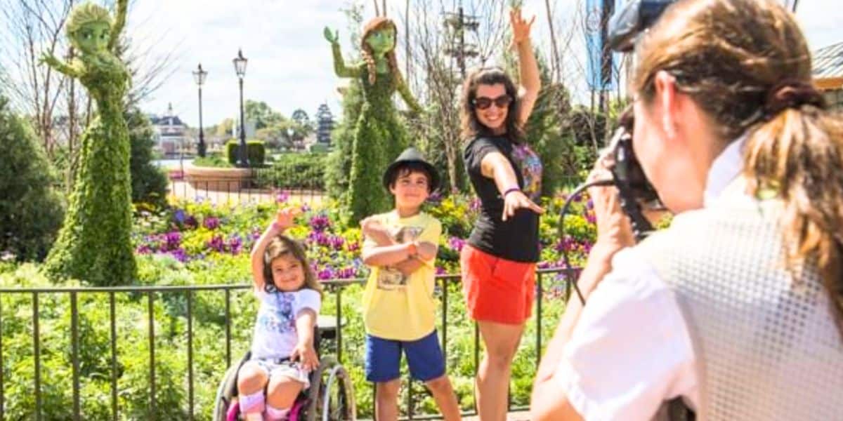 a young guest in a wheelchair takes a picture with her family at EPCOT