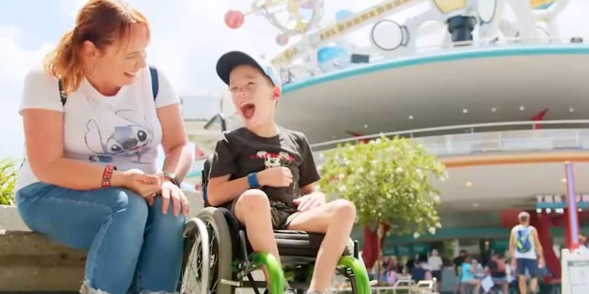 a young guest in a wheelchair enjoys a day at magic kingdom with his mom
