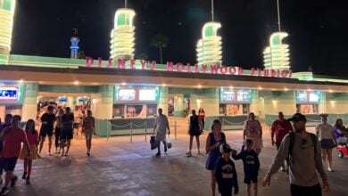 Guests stroll beneath the vibrant neon lights at the entrance to Disney’s Hollywood Studios