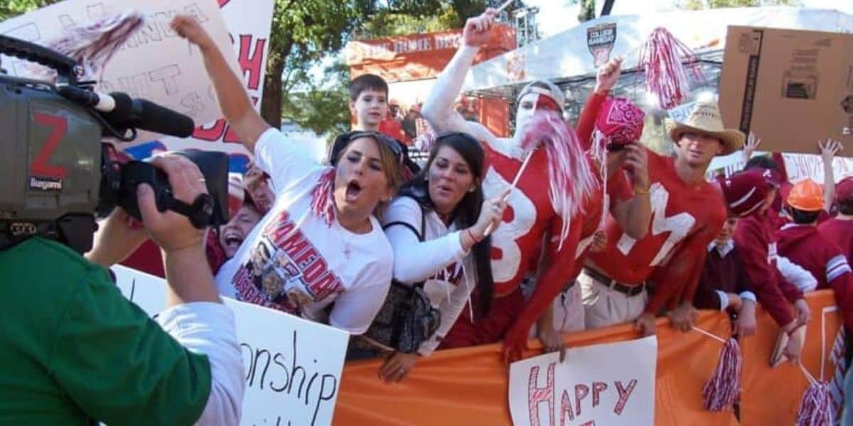 Fans decked out in their college team gear and vibrant body paint cheer wildly and wave pom-poms just beyond the orange barrier, bringing an energy to the stadium that matches the electrifying performances seen at major theme park events and live entertainment spectaculars.