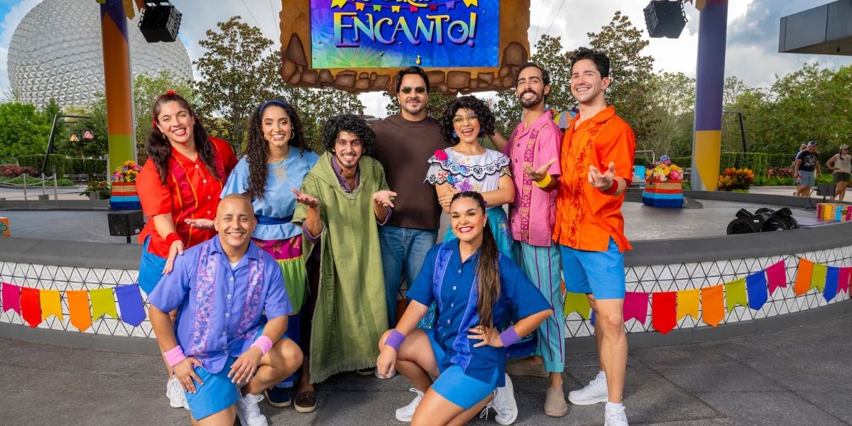 The cast of “Encanto” lights up the stage in vibrant costumes, smiling for fans in front of a colorful “Encanto” sign and festive decorations, as Walt Disney World celebrates Hispanic and Latin American Heritage Month.