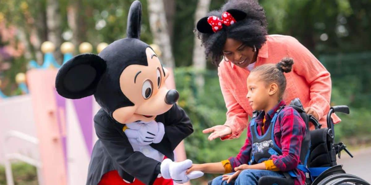Mickey Mouse interacts with a young guest in a wheelchair in Disney theme park