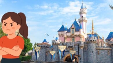 A spirited girl stands in front of Sleeping Beauty Castle, its vibrant blue rooftops gleaming under a clear sky, subtly reflecting the range of cast member experiences that Disney park fans know exist beyond the magic.