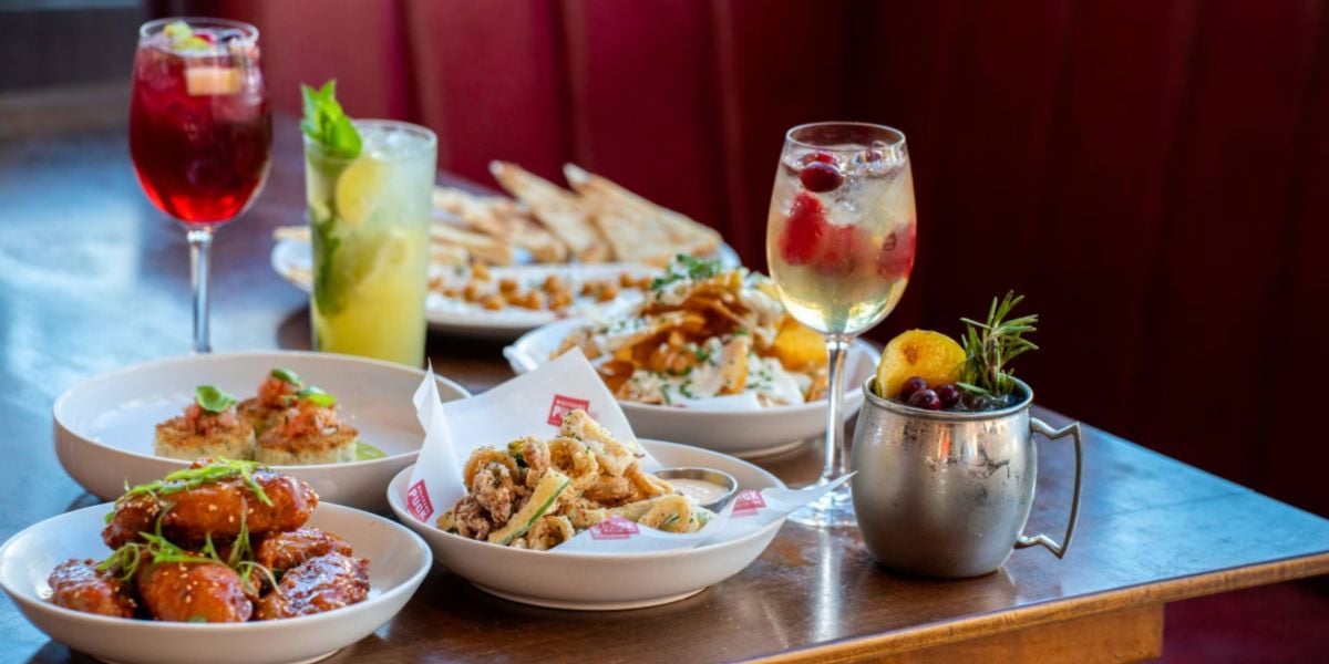 A vibrant spread of appetizers and colorful drinks in unique glasses set atop a wooden table, evoking the energetic Disney Springs vibe and perfect for guests seeking an immersive theme park dining experience.