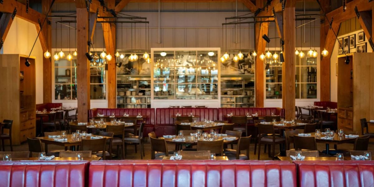 Beloved Disney Springs restaurant interior featuring vibrant red booths, polished wooden tables, stylish hanging lights, and expansive kitchen-view windows—an iconic eatery that longtime fans fondly remember before its recent closure, as highlighted in Disney news.