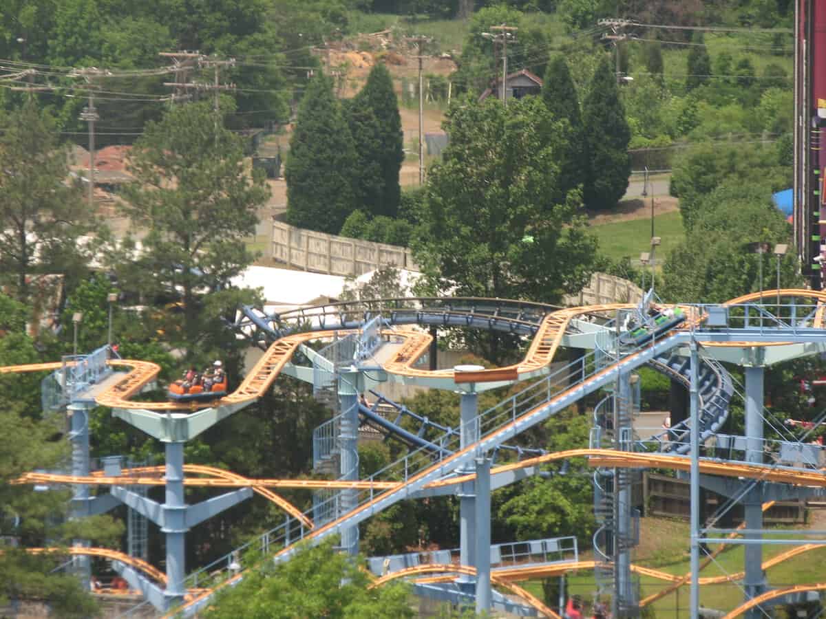A roller coaster with yellow tracks and blue supports on the park midway at Carowinds.