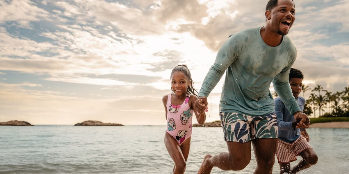 A father and his two children playing in the ocean at Aulani, A Disney Resort & Spa.