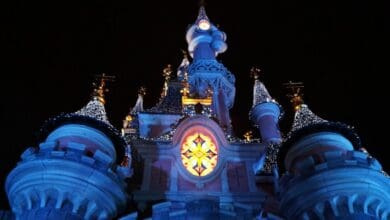 Sleeping Beauty Castle at Disneyland Paris at night, decorated with holiday lights.
