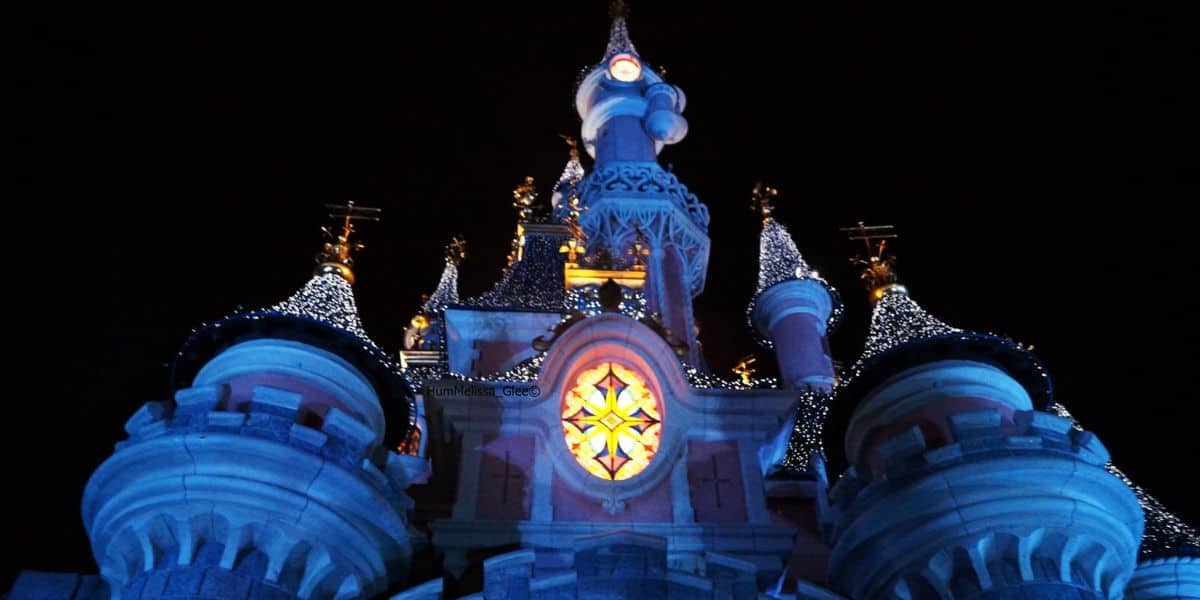 Sleeping Beauty Castle at Disneyland Paris at night, decorated with holiday lights.