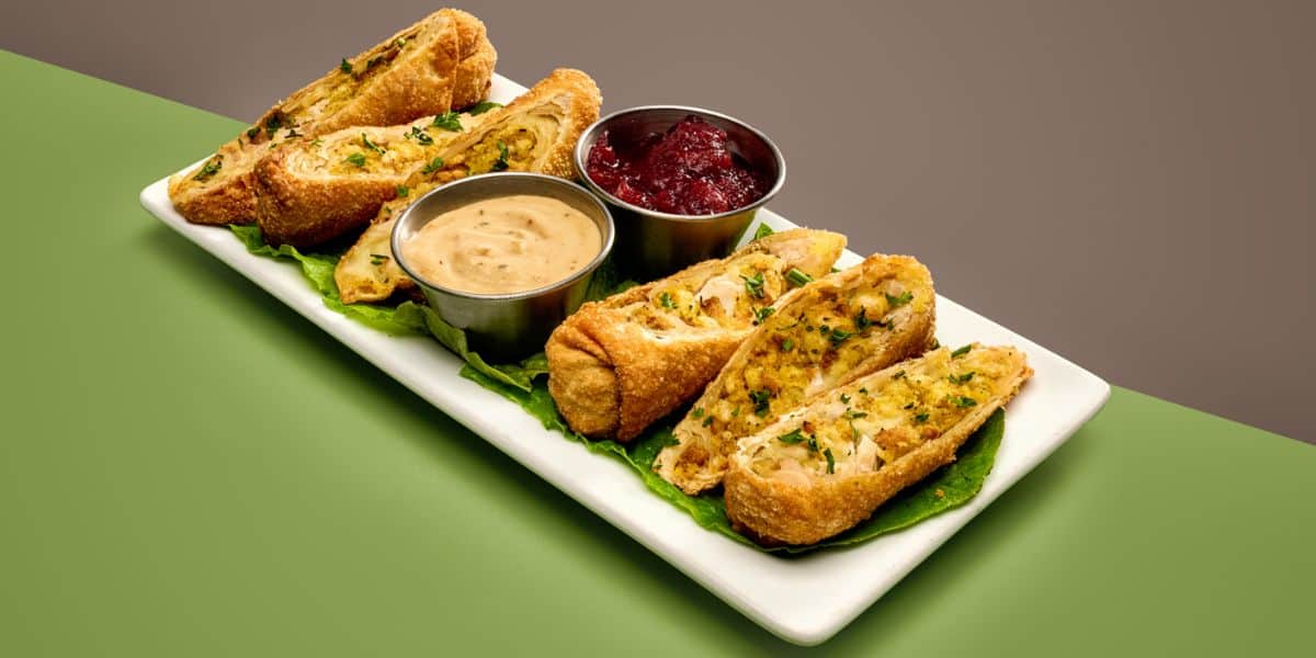 Turkey and stuffing egg rolls served with dipping sauces on a rectangular plate, a festive snack at Disney World.