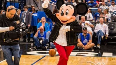 Mickey Mouse waves to fans on the Orlando Magic court at the Kia Center as a cameraman captures the magic.