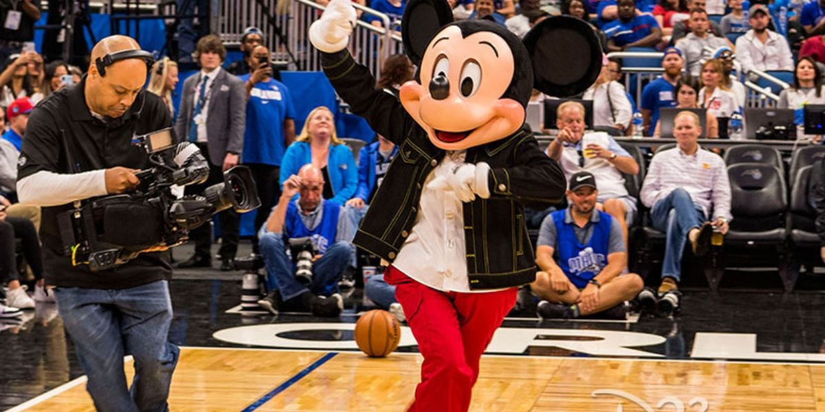 Mickey Mouse waves to fans on the Orlando Magic court at the Kia Center as a cameraman captures the magic.